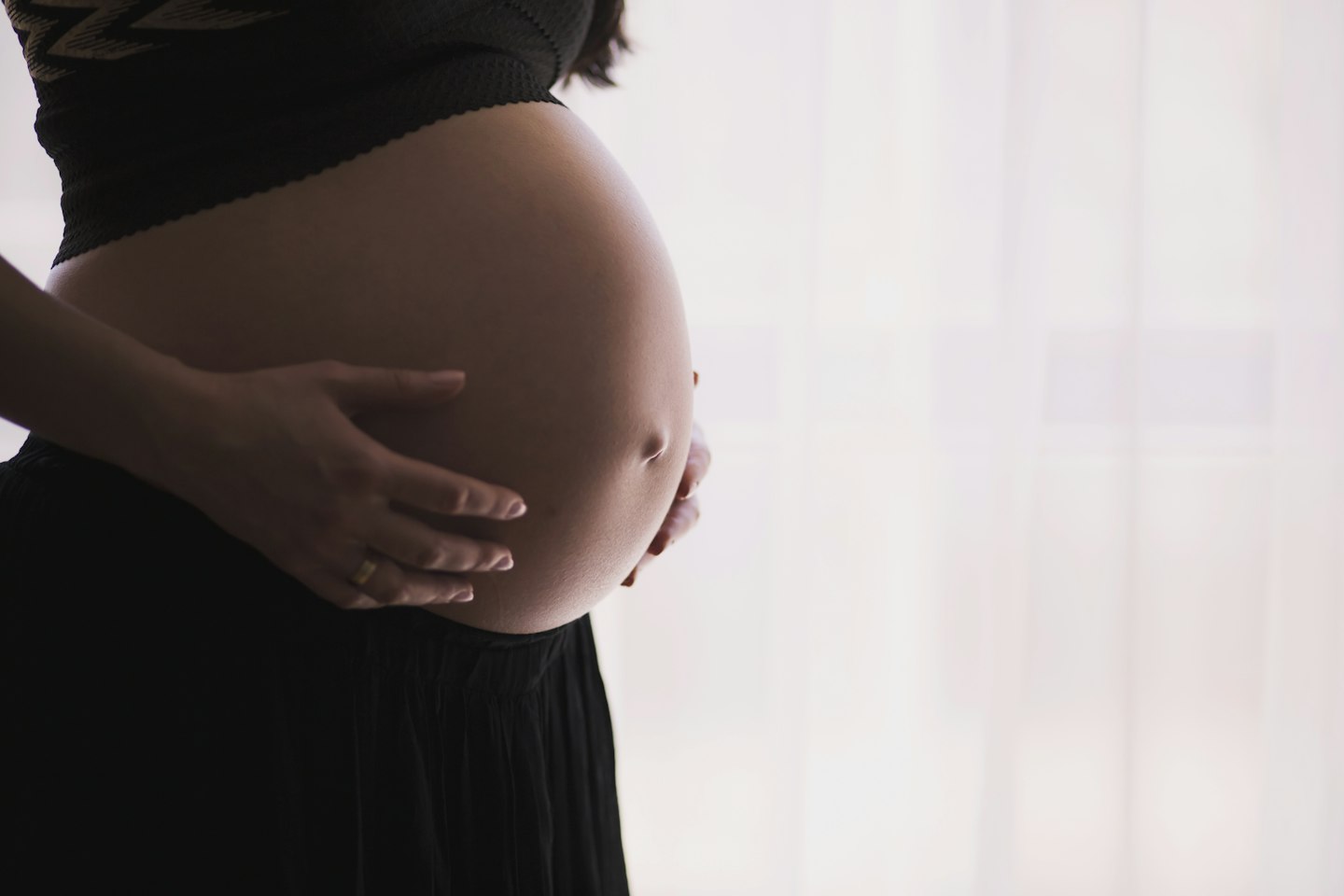 Pregnant woman resting her hands on her belly in soft window light